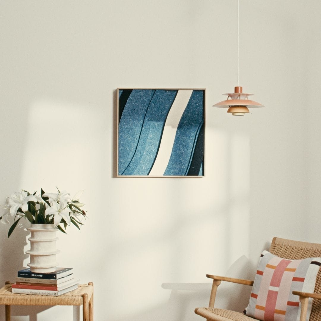 Decorative acoustic tile with blue wave design, framed in wood, enhancing sound absorption in a modern living room.